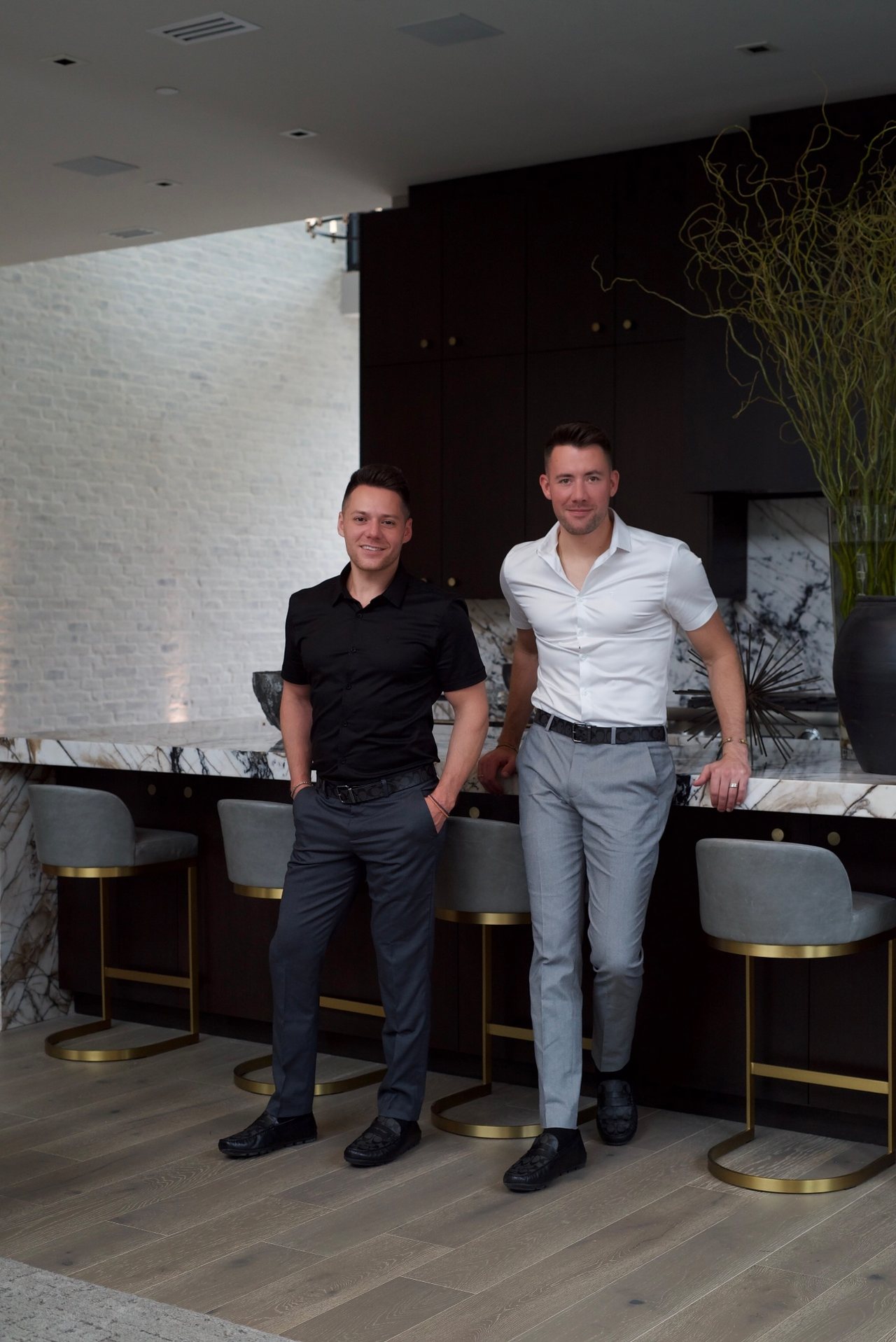 Spiro, in a black shirt and Tyler Booth, in a white shirt, the TyRo mortgage team, standing together in a modern kitchen.